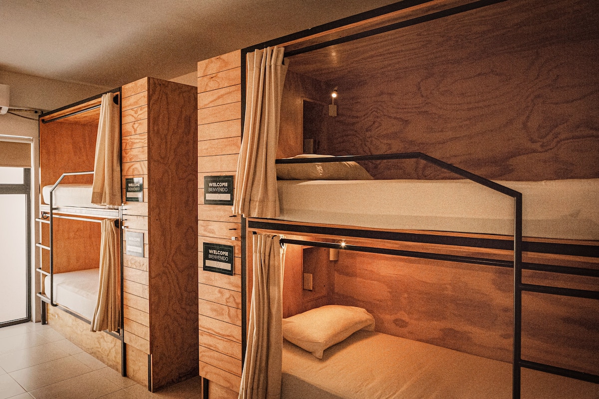 Une chambre avec des lits superposés, des panneaux de bois au mur, un panneau d’accueil et une petite table.
