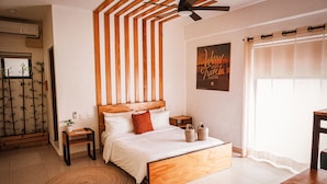A bedroom with a wooden bed, a ceiling fan, a bedside table with a lamp, a small plant, and a window with curtains. - Nomads Hotel & Rooftop pool (Cancun)