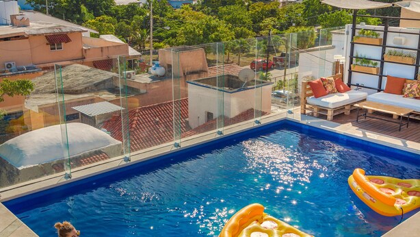 A rooftop pool with two women sitting on the edge, surrounded by wooden deck and lounge chairs. - Nomads Hotel & Rooftop pool (Cancun)