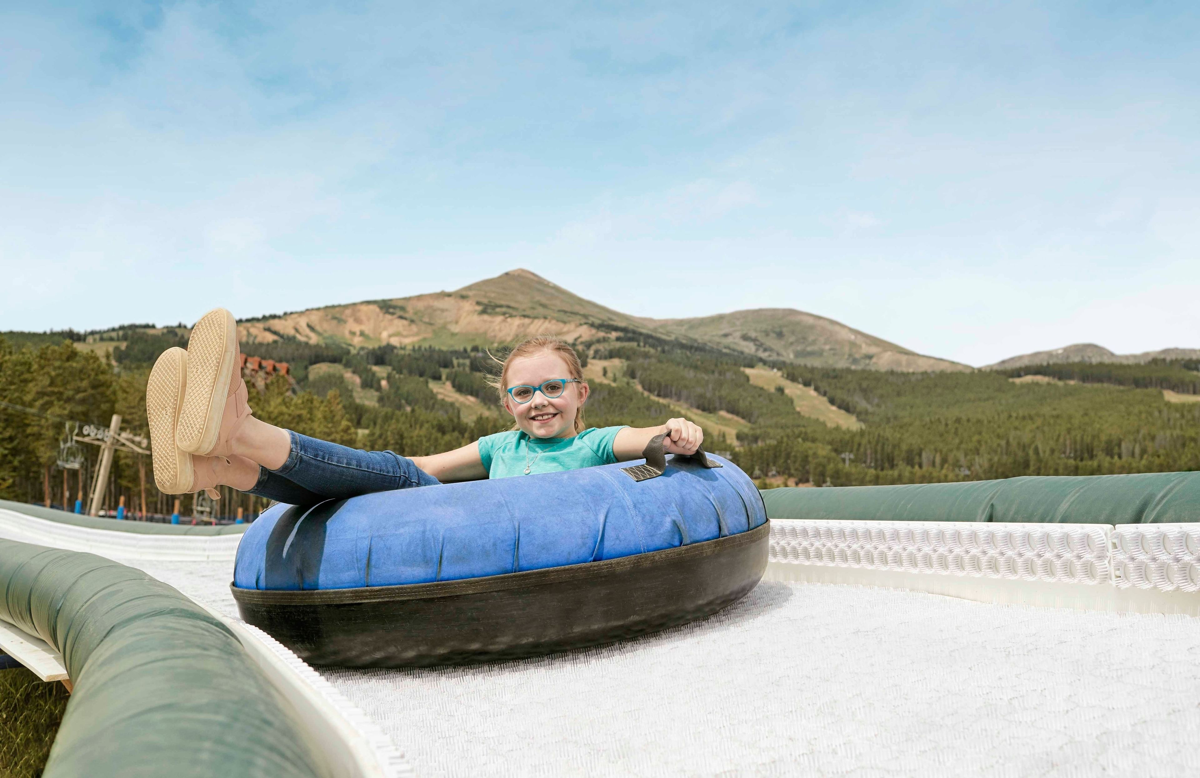 A person lying on a blue inflatable tube on a grassy area with a mountain in the background.