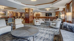 A spacious lobby with a large round table, several sofas, and armchairs. There is a wooden cabinet and a Christmas tree.