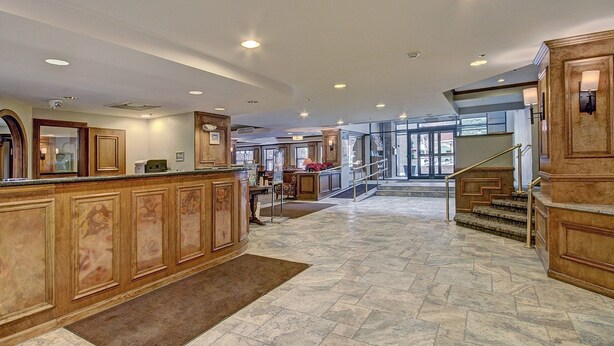 A spacious lobby with a marble floor, wooden reception desk, and a staircase leading to upper floors.