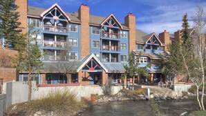 A multi-story hotel with balconies, a river in the foreground, and a clear sky.