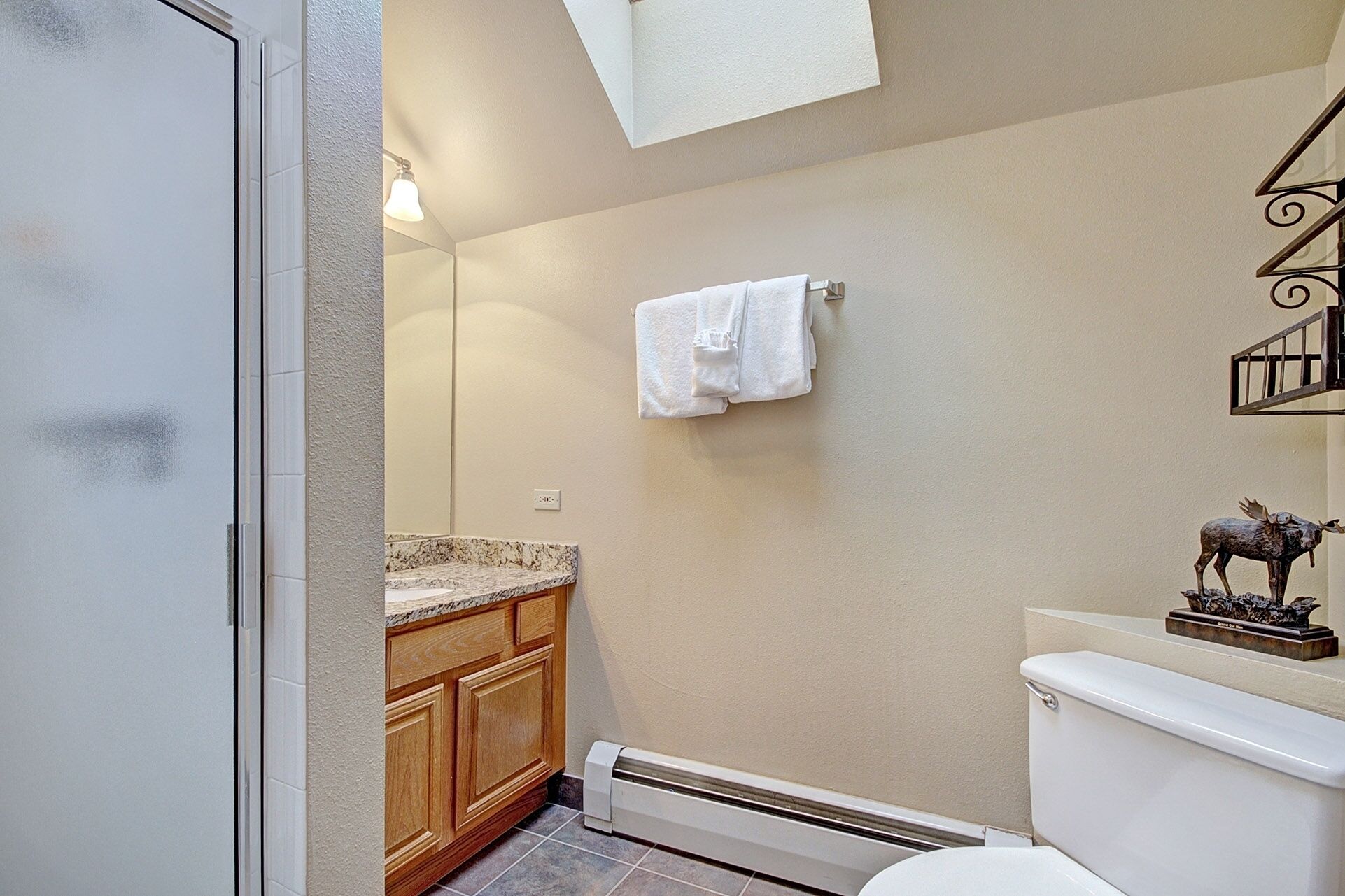 Un baño con inodoro, lavamanos con encimera de granito, armarios de madera, toallero y una estatua decorativa de alce.