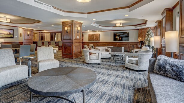 Eine geräumige Lobby mit einem großen runden Tisch, mehreren Sofas und Sesseln. Man sieht einen Holzschrank und einen Weihnachtsbaum.