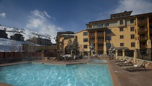 Area piscina di un hotel con acqua cristallina, lettini e una montagna innevata sullo sfondo.