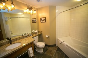 A bathroom with a granite countertop sink, a toilet, a bathtub, and a shower. There are two framed pictures on the wall, a towel rack, and a mirror above the sink.
