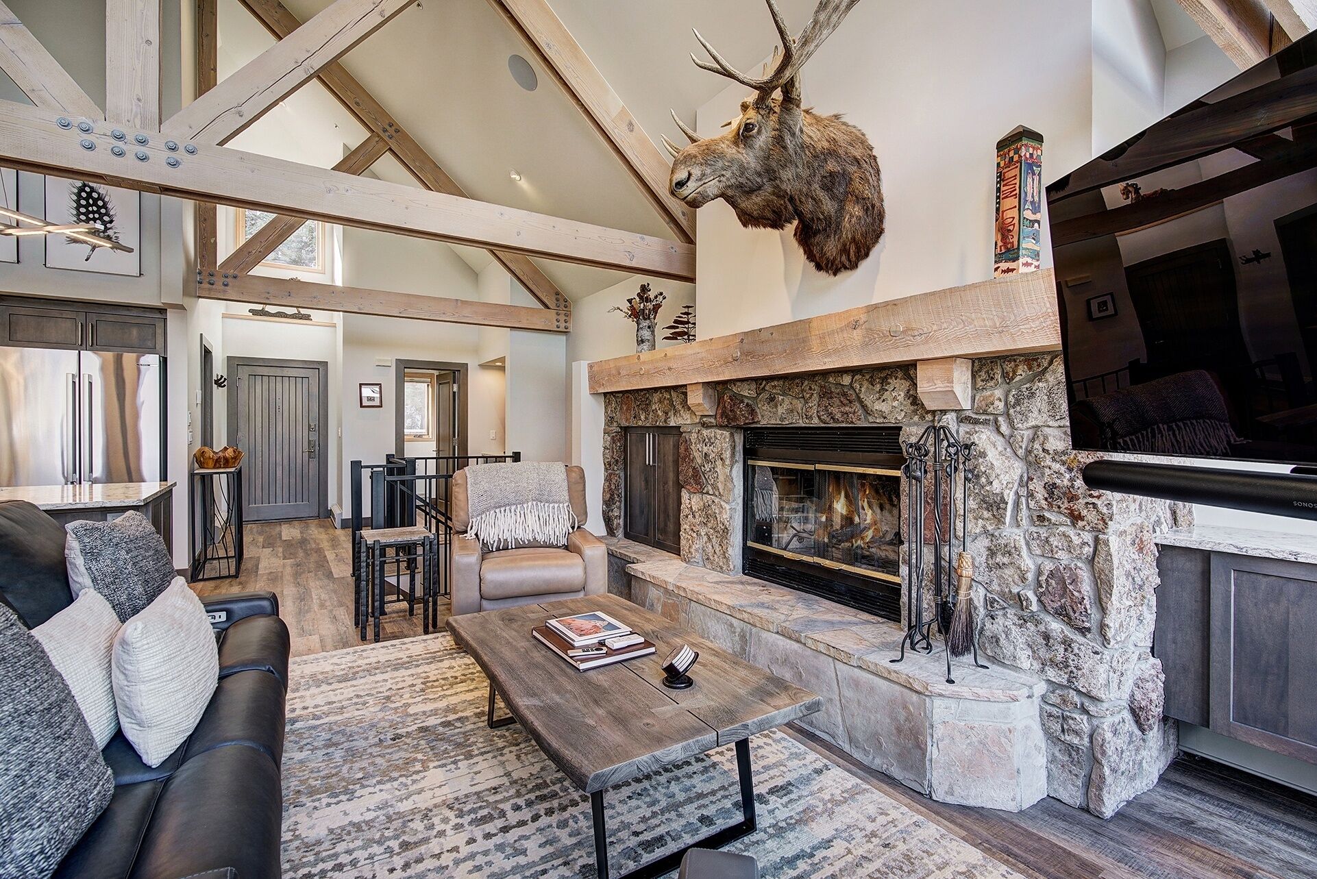A spacious living room with a stone fireplace, a mounted deer head, and a cozy seating area with a coffee table.