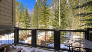 A balcony with a metal table and chairs, overlooking a snowy landscape with trees.