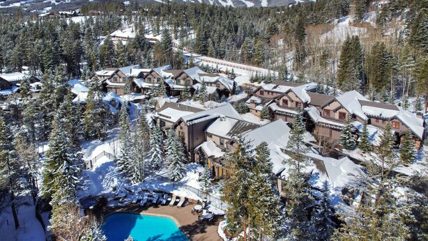 A resort with multiple chalet-style buildings, a swimming pool, and a ski lift visible in the background.