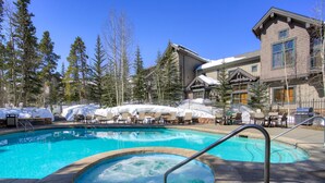 A swimming pool with a hot tub, surrounded by lounge chairs and a covered seating area, with a building in the background.