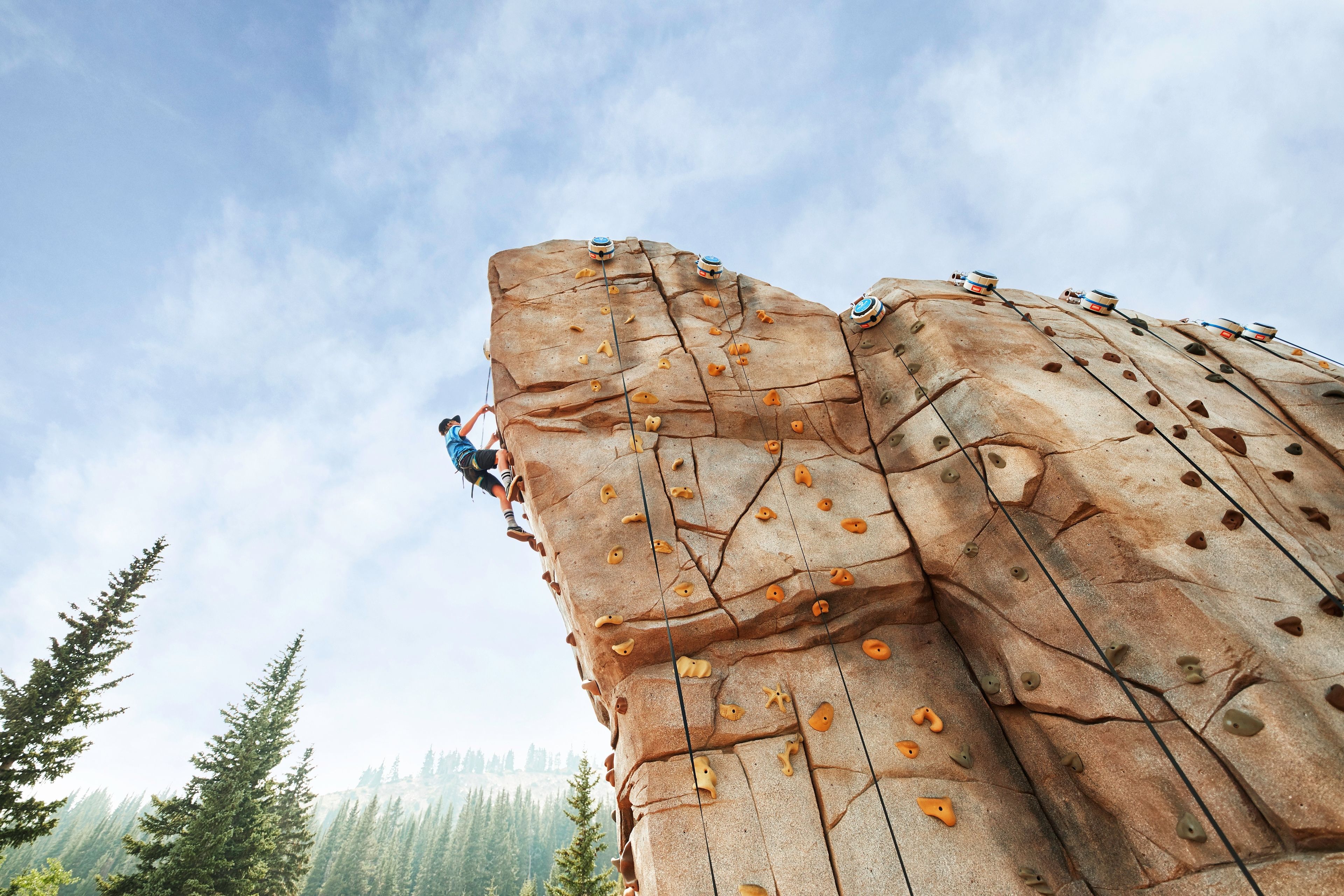 A person climbing a large rock wall with climbing holds.