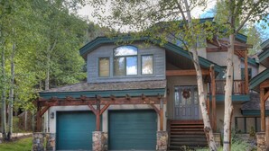 A two-story house with a green garage door, stone pillars, and a wooden pergola. - Arrowhead 254 (Edwards)