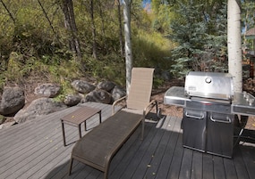 Una terraza al aire libre con una parrilla, una silla y una mesa.