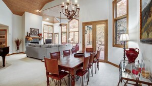 A spacious dining area with a wooden table and chairs, a chandelier, and large windows offering views of the outdoors. - Arrowhead 254 (Edwards)