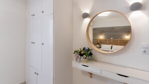 A bathroom with a white vanity, a round mirror, and a wall-mounted light fixture. - Castello Apartments (Mylopotamos)