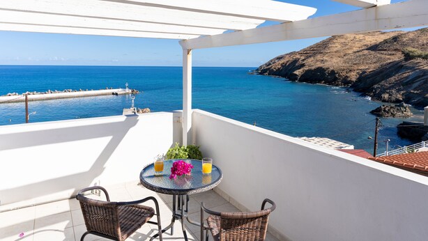 A balcony with a view of the sea, a table with drinks, and wicker chairs. - Castello Apartments (Mylopotamos)