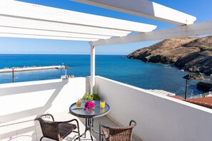 Un balcón con vista al mar, una mesa con bebidas y sillas de mimbre.