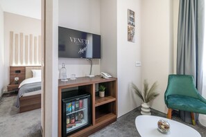 Une chambre d’hôtel avec un lit, une télévision, un minibar, un fauteuil vert et une petite table.