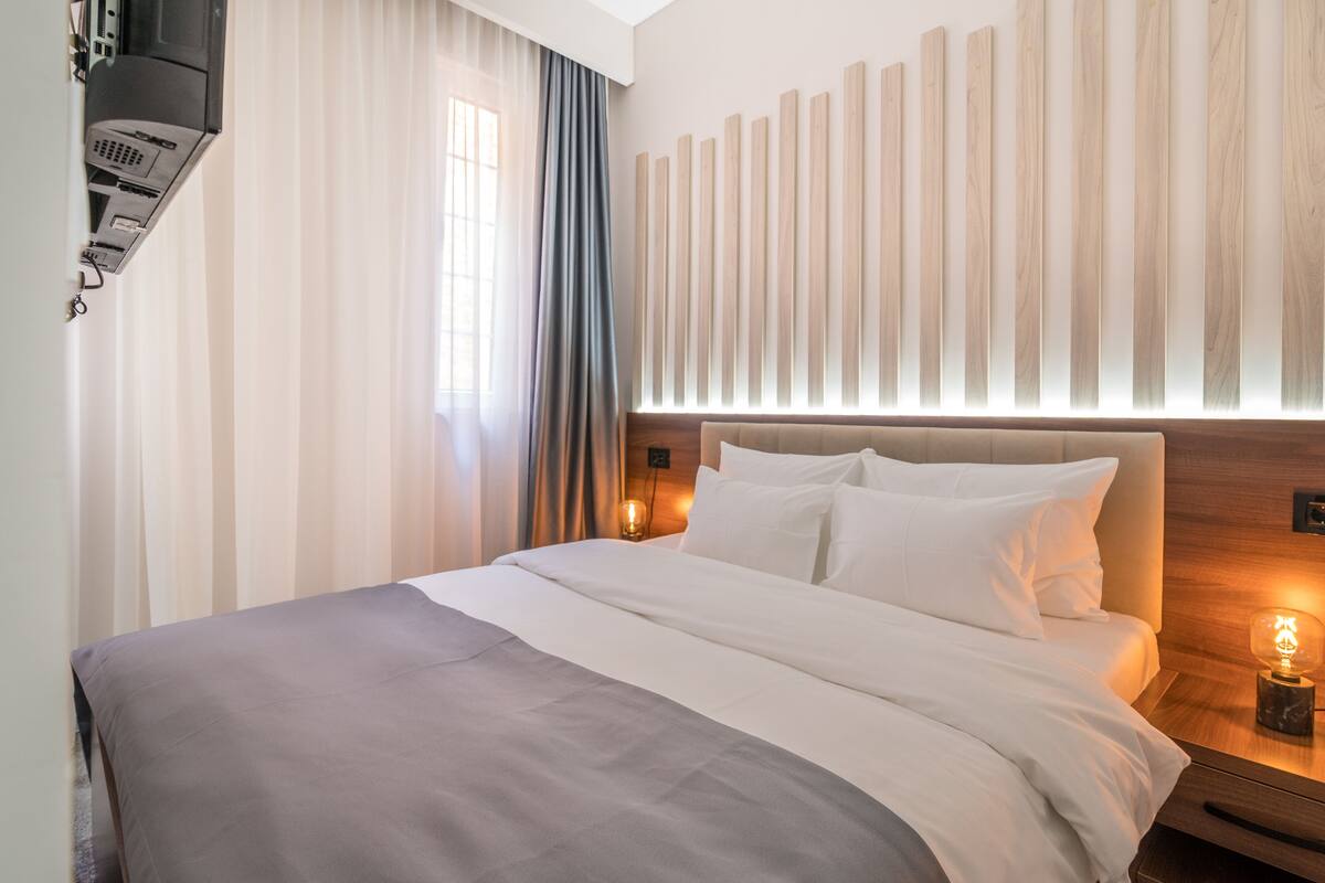 A modern hotel room with a large bed, a wooden headboard, and a bedside table with a lamp.