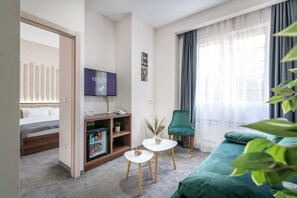 Een hotelkamer met een bed, een televisie, een tafeltje met een plant, een groene stoel en een bank.
