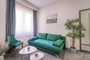 Un sofá verde, un sillón verde, dos mesas de centro blancas, una planta en maceta y un cuadro en la pared.