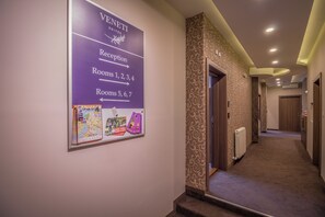Pasillo de hotel con cartel de recepción, flechas direccionales a las habitaciones y piso alfombrado.