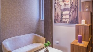 A modern living room with a sofa, a coffee table, a potted plant, a wall-mounted shelf with candles, and a cityscape painting.