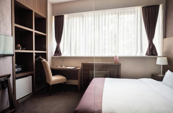 Habitación de hotel con cama, escritorio, silla, armario y ventana con cortinas.