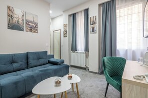 A modern living room with a sofa, two small tables, a green armchair, and a window with curtains. - Veneti Suites (Belgrade)