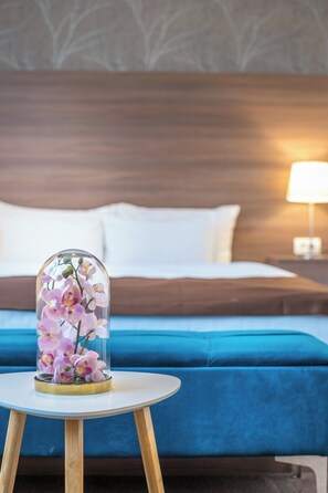 A bed with a headboard, a bedside lamp, and a table with a glass dome containing flowers.
