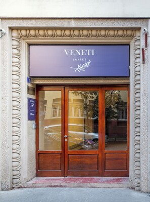 A building entrance with a sign reading 'VENETI SUITES' and a door with a glass panel.