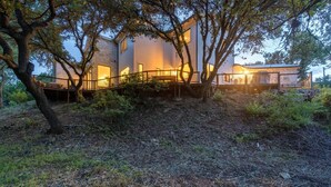 Une maison moderne dotée d’une terrasse couverte et de grandes fenêtres, entourée d’arbres et d’un paysage naturel.