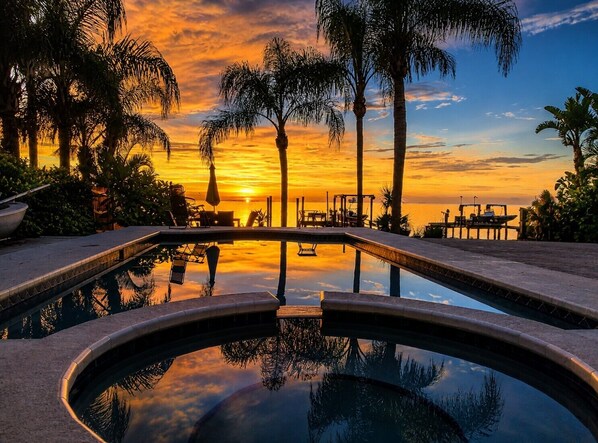 Une piscine avec vue sur le coucher de soleil, des palmiers et du mobilier dâextĂ©rieur.
