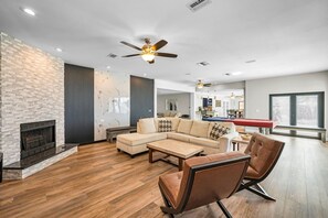 Un salon moderne avec un canapĂ© dâangle, des fauteuils en cuir, une cheminĂ©e et un ventilateur de plafond.