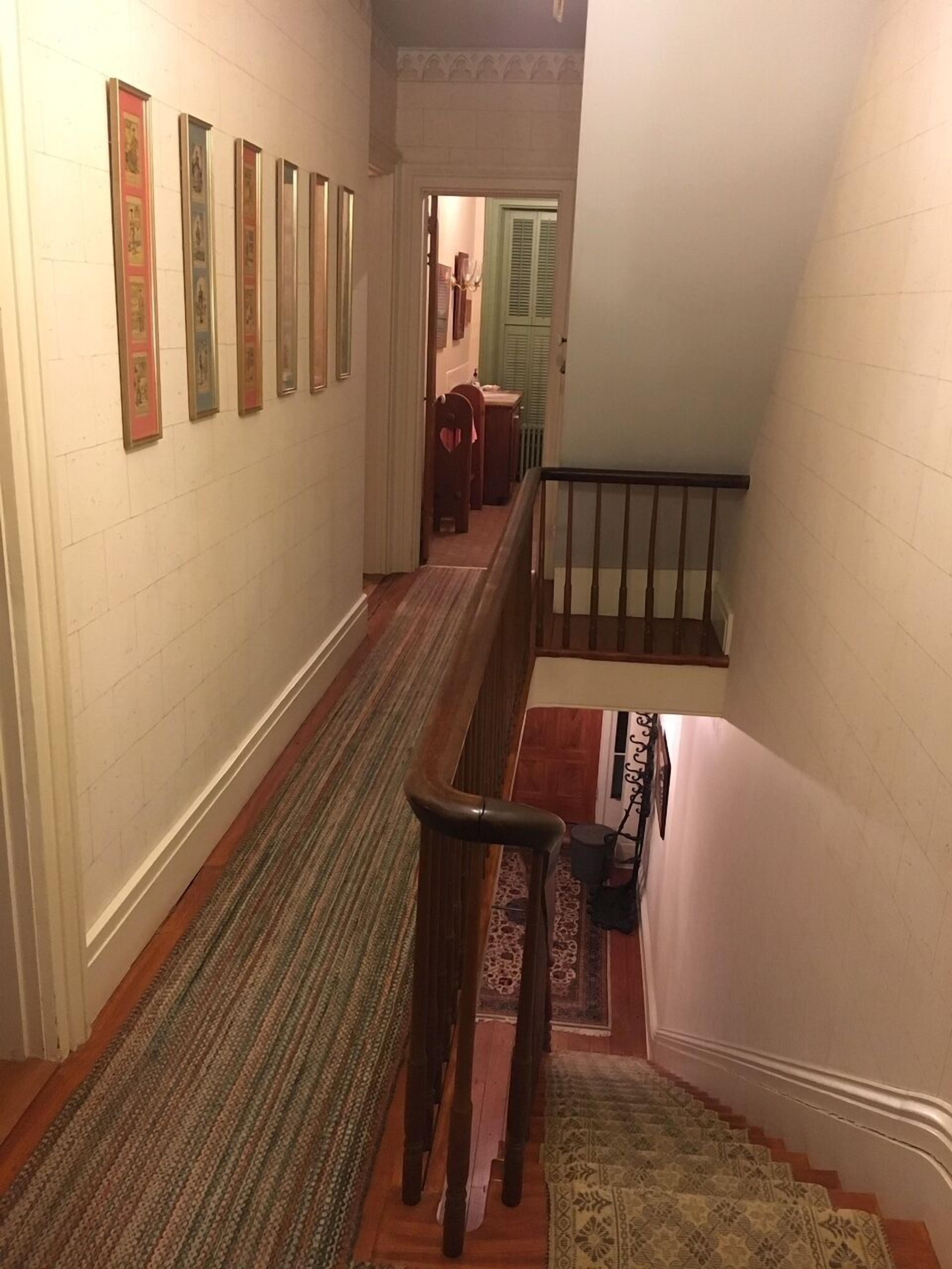 A hallway with a wooden bench, a staircase with a railing, and a patterned rug.