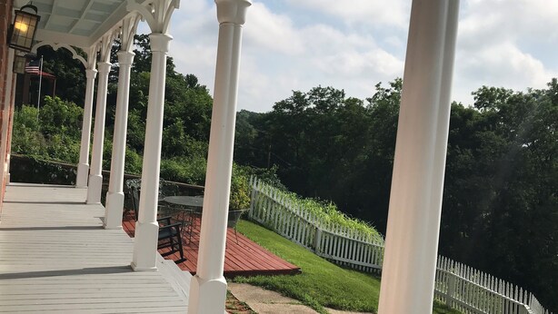 A covered porch with white columns and a view of a green landscape. - View from Quality Hill overlooking historic district, quick walk to downtown (Galena)