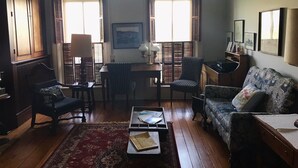 A living room with wooden flooring, a red patterned rug, a sofa, a chair, a table, and two windows with shutters. - View from Quality Hill overlooking historic district, quick walk to downtown (Galena)