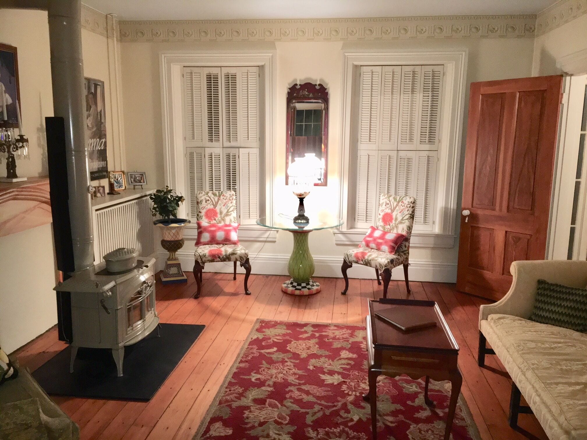 A cozy living room with two floral armchairs, a wooden coffee table, a vintage stove, and a red patterned rug.