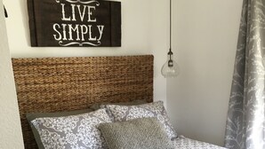 Ein Schlafzimmer mit einem gemusterten Bettbezug, einem gewobenen Kopfteil, einem Schild mit der Aufschrift 'LIVE SIMPLY' und einer Pendelleuchte.