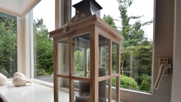 Een houten lantaarn met een glazen omhulsel op een vensterbank.
