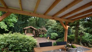 Een houten pergola met een tafel en stoelen in een tuin.