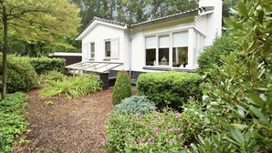 Een wit huis met een schuin dak, grote ramen en een overdekt terras.