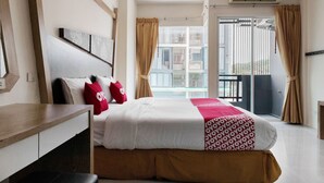 A hotel room with a large bed, a wooden desk, a window with curtains, and an air conditioning unit. - OYO 792 Omsaga Phuket Hotel (Ratsada)
