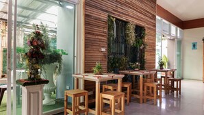 A restaurant with wooden tables and chairs, a large window with plants, and a view of the outdoors. - OYO 792 Omsaga Phuket Hotel (Ratsada)