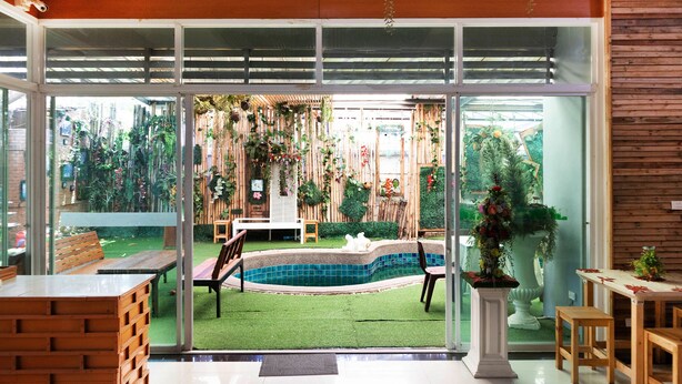 A modern interior with a glass door leading to a backyard with a swimming pool, outdoor furniture, and a wooden fence. - OYO 792 Omsaga Phuket Hotel (Ratsada)