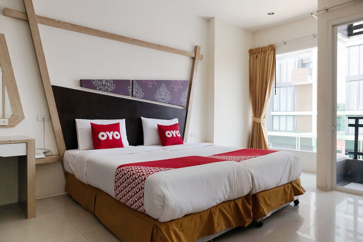 Una cama bien hecha con cabecera, mesita de noche y ventana con cortinas.