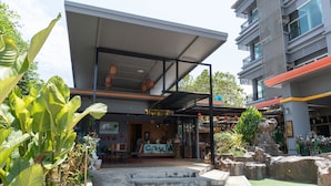 A modern building with a covered entrance, outdoor seating, and a small garden area. - OYO 792 Omsaga Phuket Hotel (Ratsada)