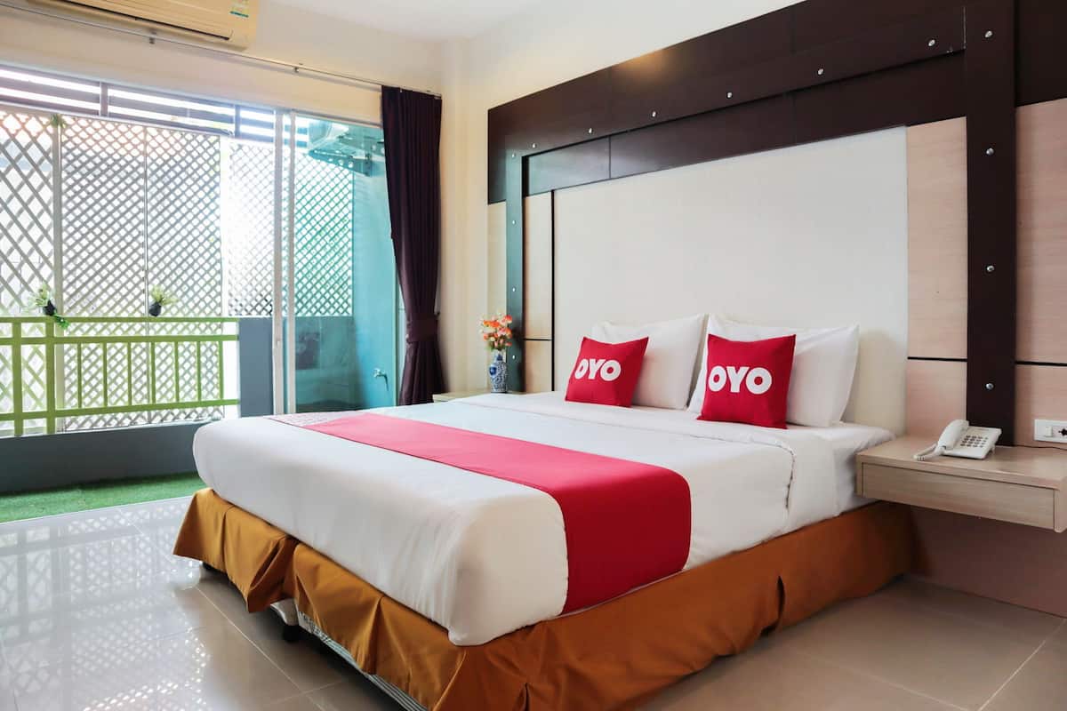 Habitación de hotel con una cama grande, un teléfono en la mesita de noche y vista a un balcón con una cerca verde.