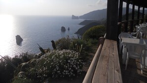 Une vue sur la côte, avec une terrasse en bois et des chaises en plastique blanches, donnant sur la mer et les falaises lointaines.